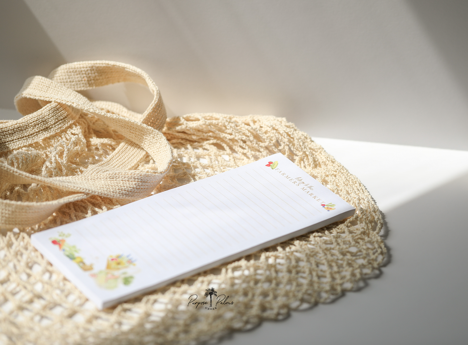 white grocery list notepad. lets go to the farmers market shown at top with fruits and vegetables on each side. lines down to the bottom. watercolor fruits and vegetables at the bottom with a mesh farmers market bag and a bouquet of flowers.